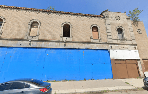 Abandoned building with boarded windows and a blue-painted lower facade, set against a clear blue sky.