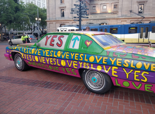 A colorful car covered in vibrant "YES" and "LOVE" graffiti parked in an urban area.