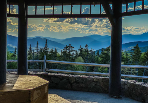 Scenic view from a gazebo overlooking mountains and trees under a cloudy sky.