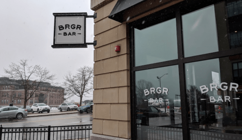 A snowy scene featuring the BRGR Bar sign and large windows, with parked cars and trees in the background.