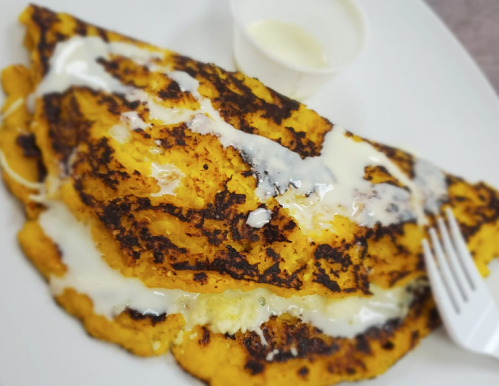 A golden-brown omelette drizzled with white sauce, served on a plate with a small cup of sauce and a fork.
