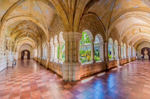 A serene stone corridor with arches, columns, and lush greenery visible through the windows, creating a tranquil atmosphere.
