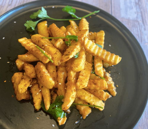 A plate of golden, seasoned crinkle-cut fries garnished with fresh cilantro on a black dish.