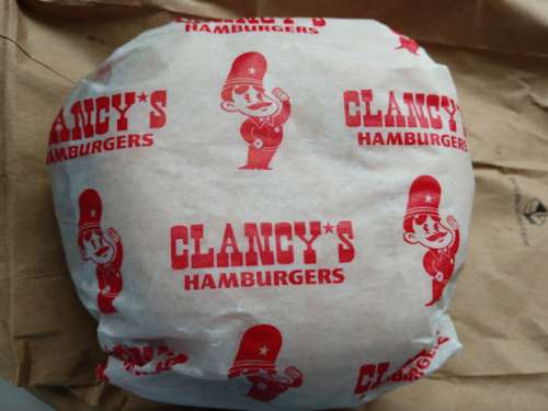 A wrapped hamburger with a red and white Clancy's Hamburgers logo on the paper.