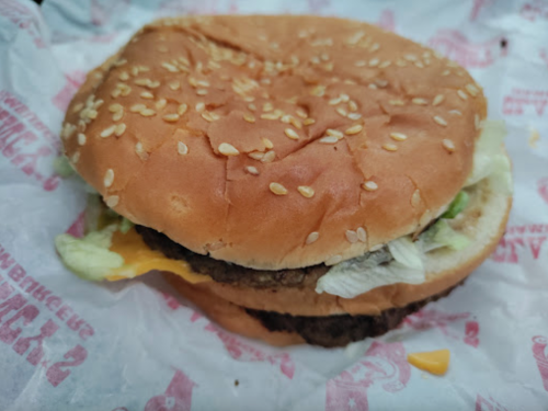 A sesame seed bun sandwich with lettuce, cheese, and two beef patties, wrapped in paper.