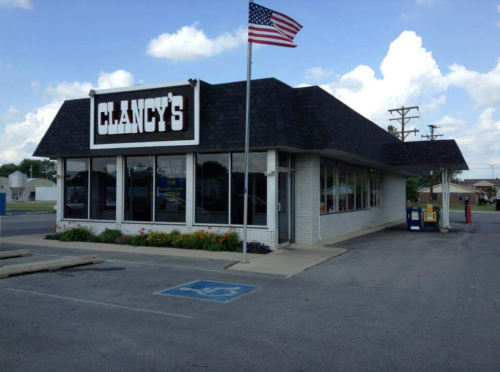 Exterior of Clancy's restaurant with a flag, featuring a large sign and flower beds in front.