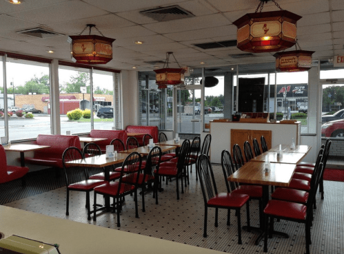 Interior of a casual dining restaurant with red booths, wooden tables, and large windows. Warm lighting from hanging lamps.