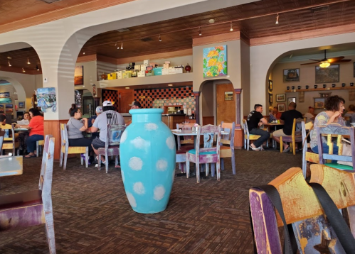 A colorful restaurant interior with diners, featuring a large blue vase in the foreground and vibrant decor.