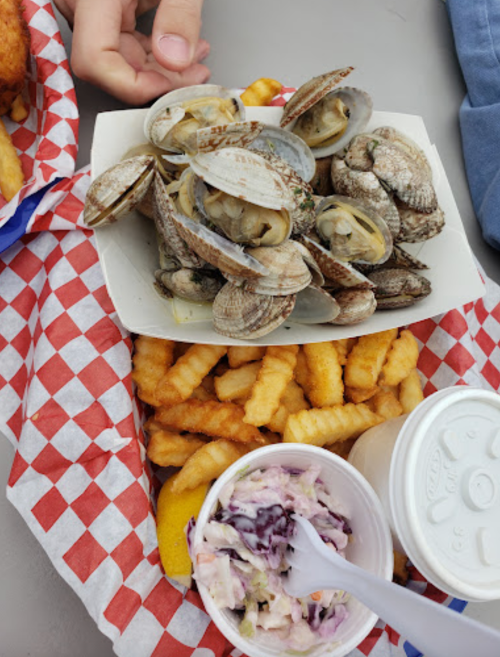 A plate of clams on a bed of crinkle-cut fries, with a cup of coleslaw and a lemon wedge on the side.