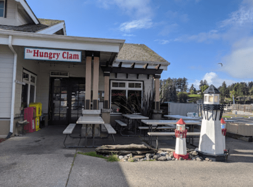 Exterior of The Hungry Clam restaurant featuring outdoor seating, a lighthouse decoration, and a clear blue sky.