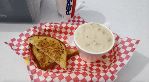 A bowl of creamy soup with herbs, served with two slices of toasted garlic bread in a red and white checkered basket.