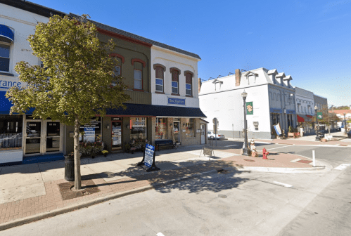 A street view of a small town with shops, trees, and clear blue skies.