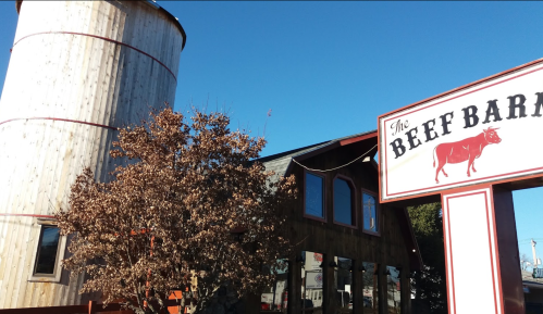A rustic building with a wooden silo and a sign reading "The Beef Barn" against a clear blue sky.