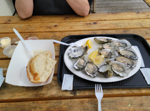 A plate of oysters with lemon slices, a roll of bread, and dipping sauces on a wooden table.