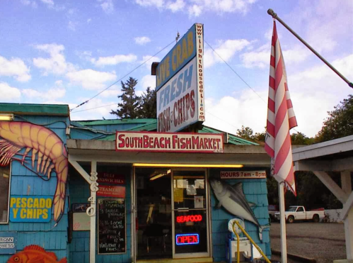 Exterior of South Beach Fish Market with colorful signage, flags, and a display of fresh seafood offerings.