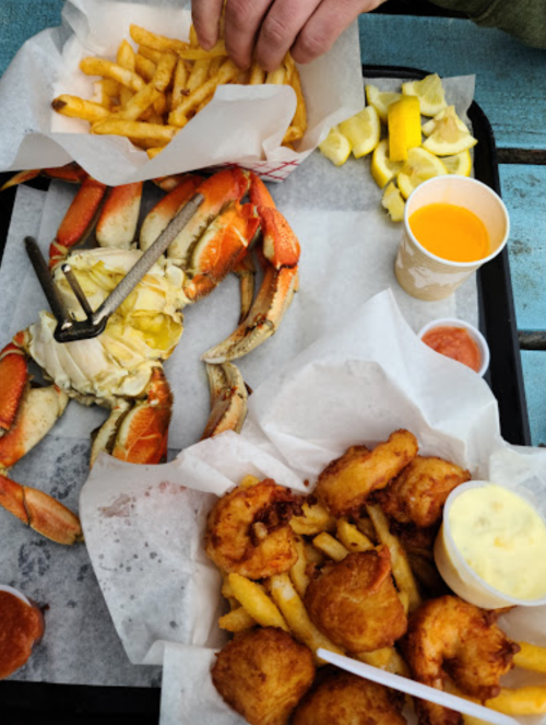 A tray of seafood featuring a large crab, fries, hush puppies, lemon wedges, and two cups of sauce and drink.
