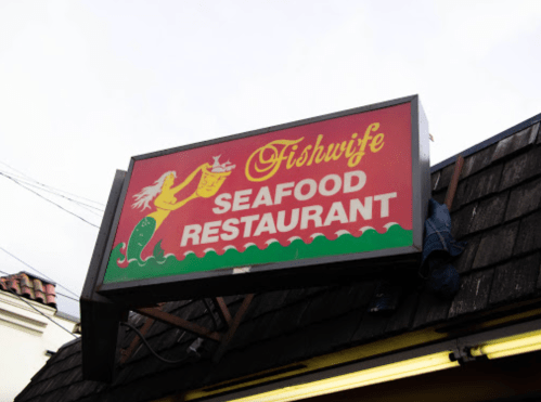 Sign for "Fishwife Seafood Restaurant" featuring a mermaid graphic, mounted on a wooden structure.