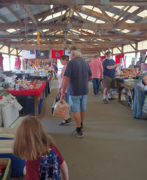 A bustling market interior with shoppers browsing various stalls and colorful flags hanging from the ceiling.