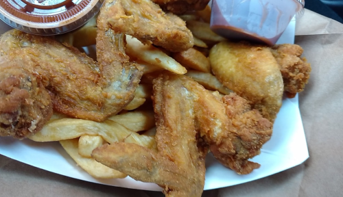 A plate of crispy fried chicken wings served with French fries and a small container of dipping sauce.