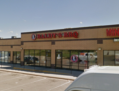 Exterior of Baldy's BBQ restaurant, featuring a brick facade and large windows, with a parking lot in front.