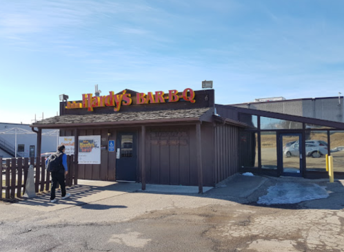 A rustic barbecue restaurant with a sign reading "Hardy's BAR-B-Q" and a person walking towards the entrance.