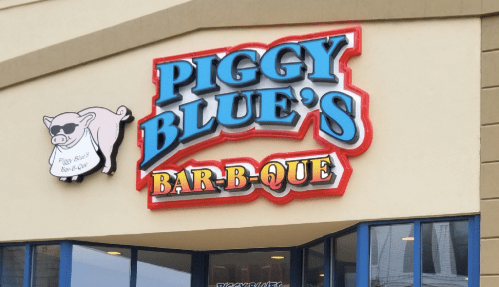 Sign for "Piggy Blue's Bar-B-Que" featuring a cartoon pig wearing sunglasses. Bright colors and bold lettering.
