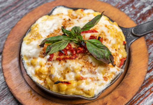 Creamy baked macaroni and cheese topped with herbs and crispy breadcrumbs in a small cast-iron skillet.