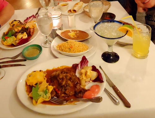 A table set with various Mexican dishes, including rice, beans, and colorful plates of food, alongside drinks.