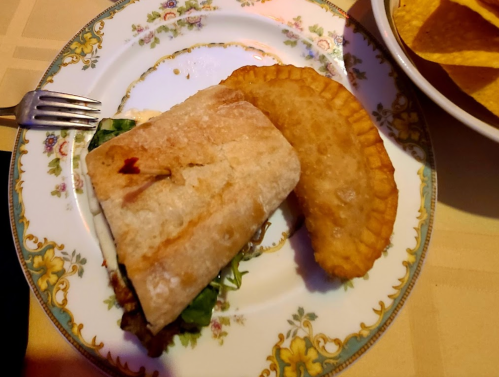 A plate with a sandwich and a fried pastry, accompanied by tortilla chips in the background.