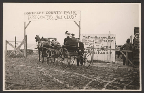 A horse-drawn carriage at the entrance of the Greeley County Fair, with signs about closing and local businesses.