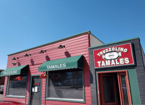 Exterior of Truzzolino Tamales restaurant with green awnings and a bright red sign, under a clear blue sky.