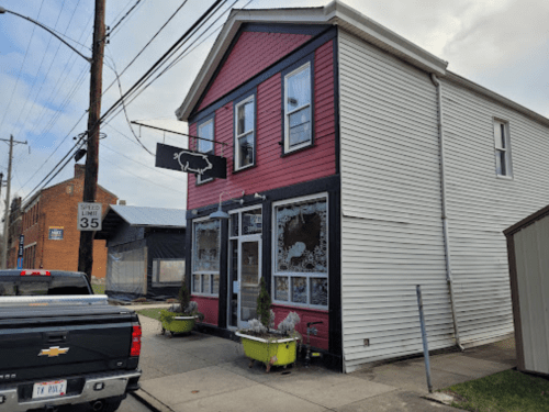 A two-story building with red and white siding, featuring a sign with a cow, surrounded by parked cars and street elements.