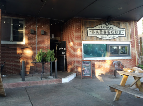 Exterior of Ray Ray's Barbecue featuring a wooden sign, patio seating, and a welcoming entrance.