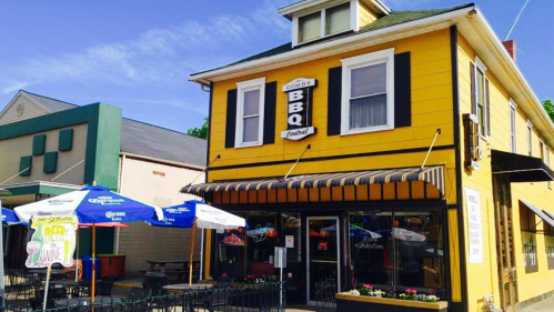 A yellow BBQ restaurant with outdoor seating and umbrellas, featuring a sign that reads "Combs BBQ Central."