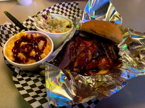A plate featuring a BBQ sandwich, coleslaw, and mac and cheese, all served in a checkered basket.
