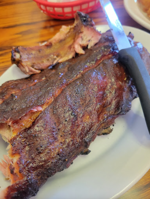 A plate of smoked ribs with a knife resting beside them, showcasing a crispy, charred exterior.