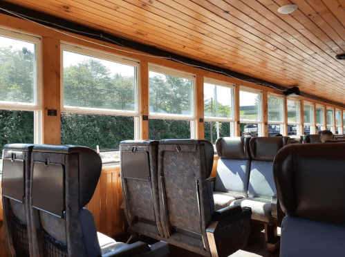 Interior of a train carriage with wooden paneling and rows of empty seats beside large windows.