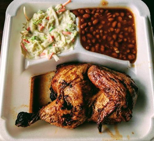 A takeout container with grilled chicken, coleslaw, and baked beans.