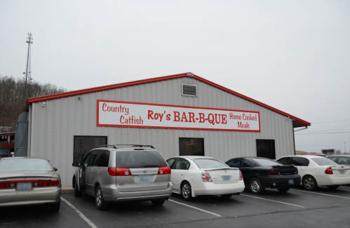 Exterior of Roy's Bar-B-Que restaurant, featuring a sign and parked cars in front on a cloudy day.