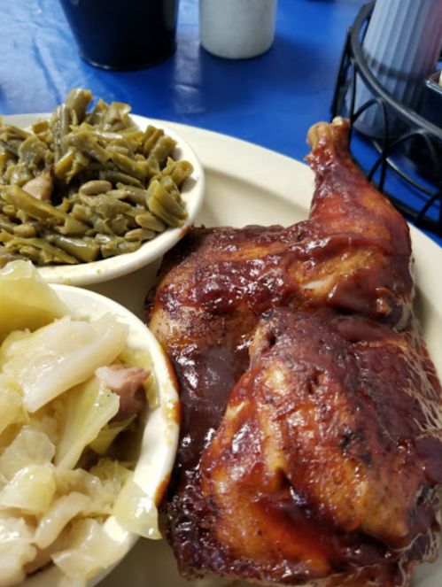 A plate featuring a glazed chicken leg, green beans, and cabbage on a blue table.