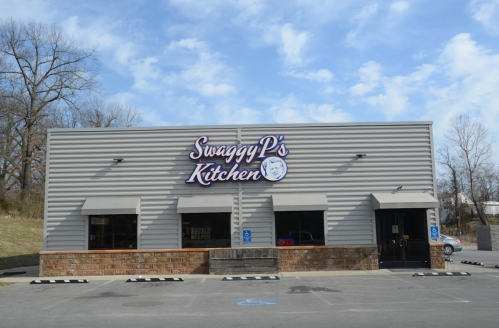 Exterior of Swaggy P's Kitchen, a casual dining restaurant with a sign and open windows under a blue sky.