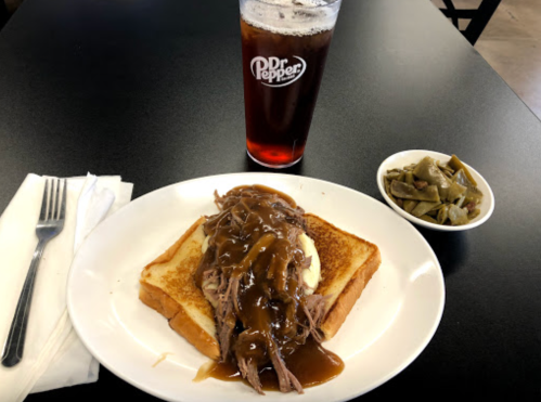 A plate with pulled pork on toast topped with gravy, a side of green beans, and a glass of Dr Pepper.