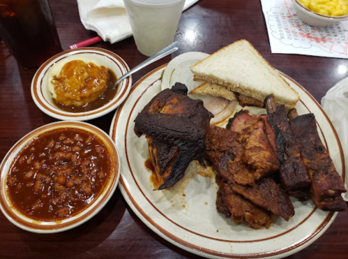 A plate of barbecue ribs, chicken, baked beans, and a side of macaroni and cheese, with slices of bread.