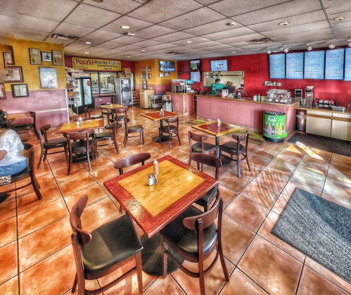 A brightly lit restaurant interior with wooden tables, chairs, and a colorful counter in the background.