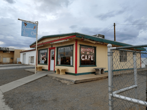 A colorful café building with a sign reading "Ramona's Café," surrounded by gravel and a chain-link fence.