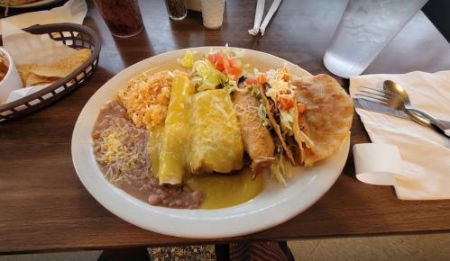 A plate of Mexican food featuring enchiladas, rice, refried beans, tacos, and a side of salad.