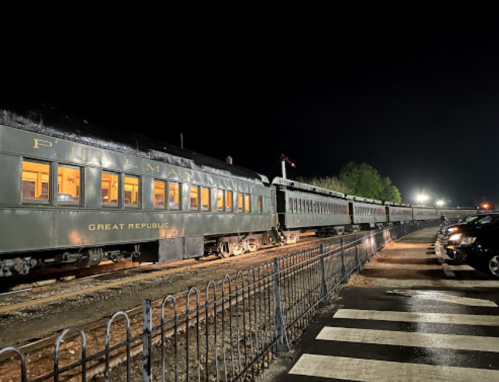 A vintage train named "Great Republic" parked at night, with cars nearby and lights illuminating the scene.