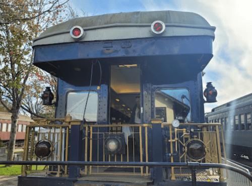 A vintage train car with a blue exterior and a rounded roof, featuring red lights and a decorative railing.