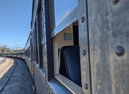 A close-up of a vintage train car with open windows, showing a curved track and clear blue sky in the background.