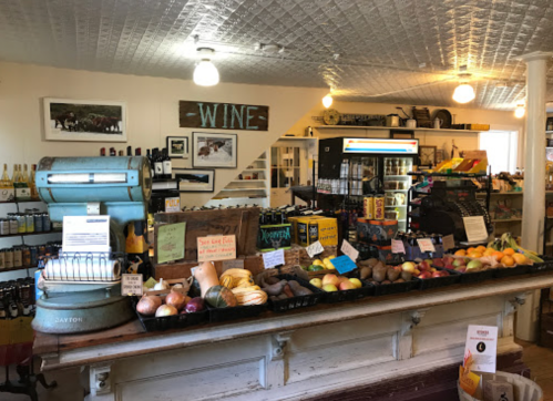 A rustic store interior featuring a variety of fruits, vegetables, and wine bottles on display.